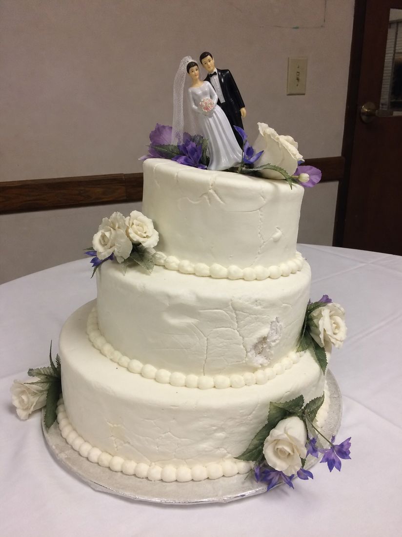 Three-tier white wedding cake with roses and a bride and groom topper